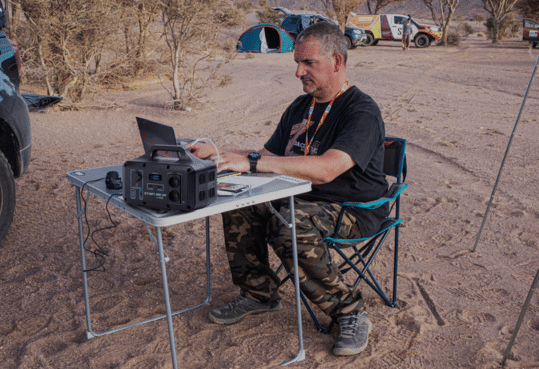 Homme assis, Batterie IZYWATT qui charge un ordinateur portable, équipement de camping, radio,