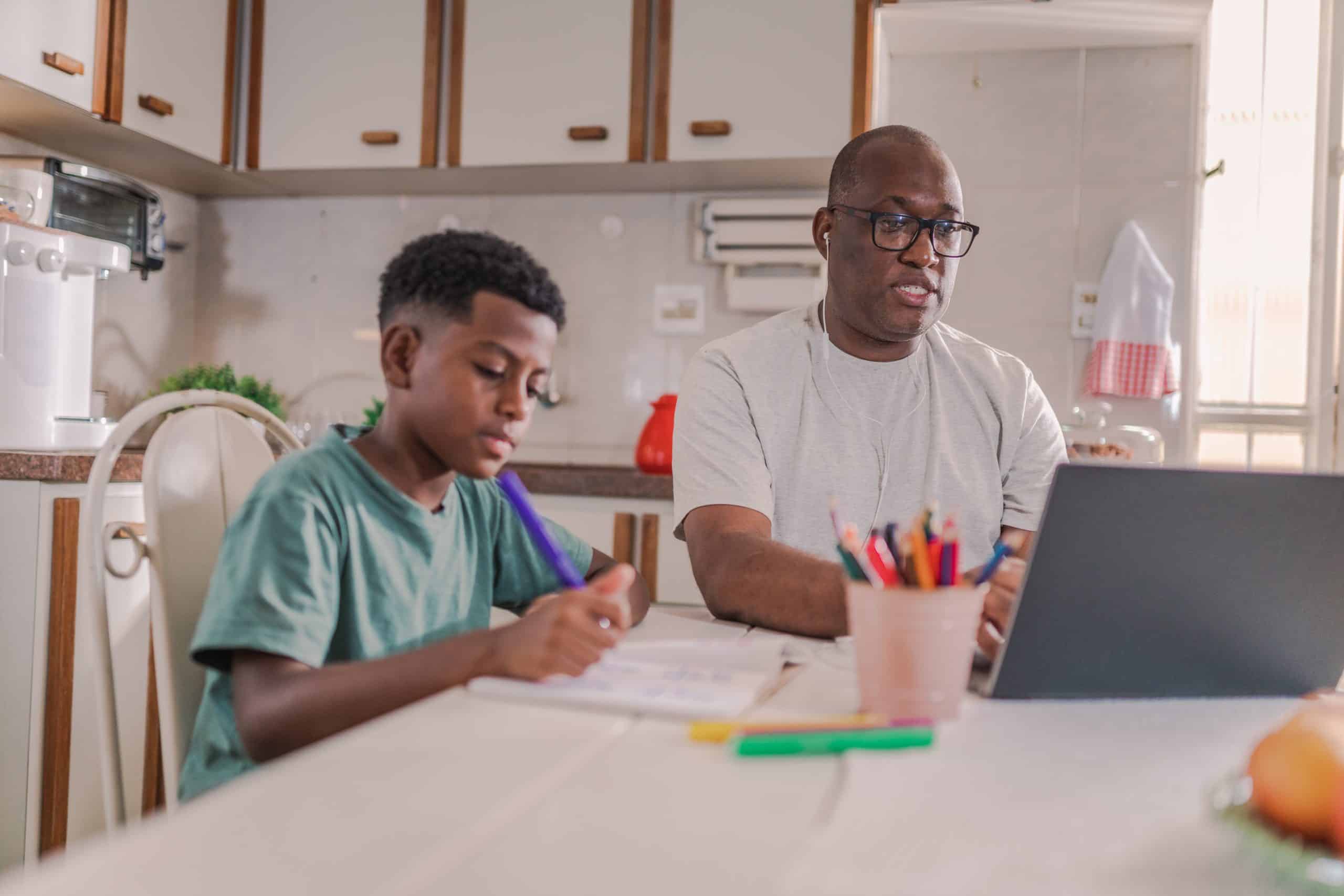Brazilian man working on laptop at the kitchen table in his home in Brazil while helping his son with his school work